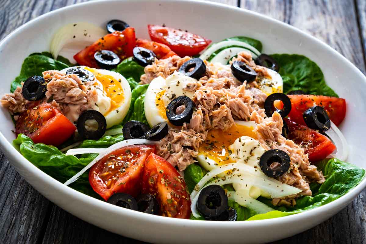Salat mit Tomaten, Oliven, Eiern, Thunfisch, Zwiebeln in einer weissen Schuessel