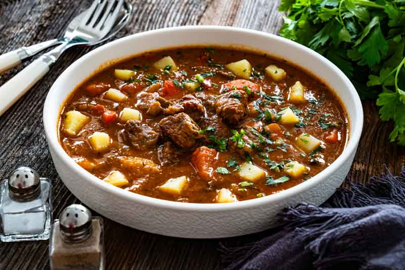 Gulaschsuppe mit Fleischstuecken, Kartoffeln, Tomaten und Petersilie auf einem Teller
