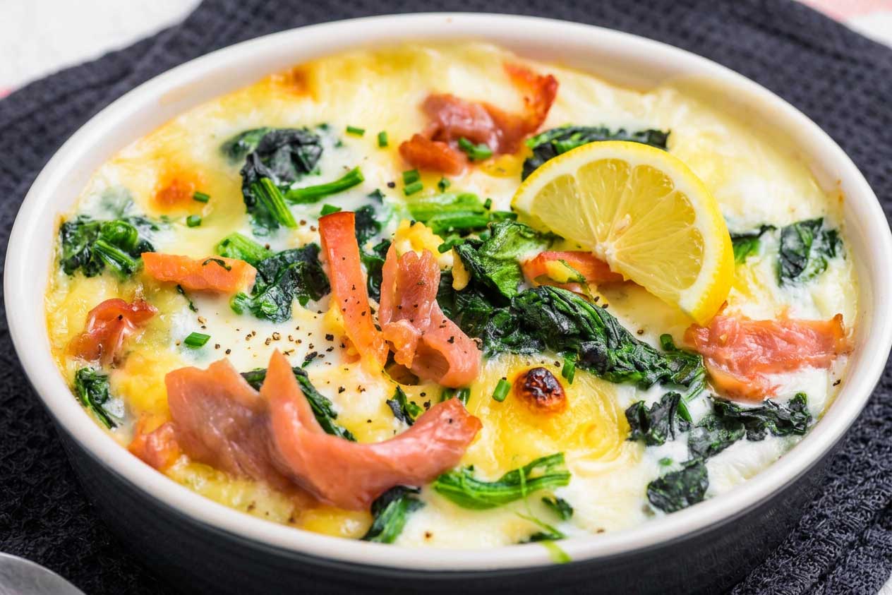 Auflaufform mit Kartoffelstuecken, Lachsstreifen, Spinat, Zwiebelstreifen mit Kaese gratiniert und mit einem Viertel Zitrone garniert