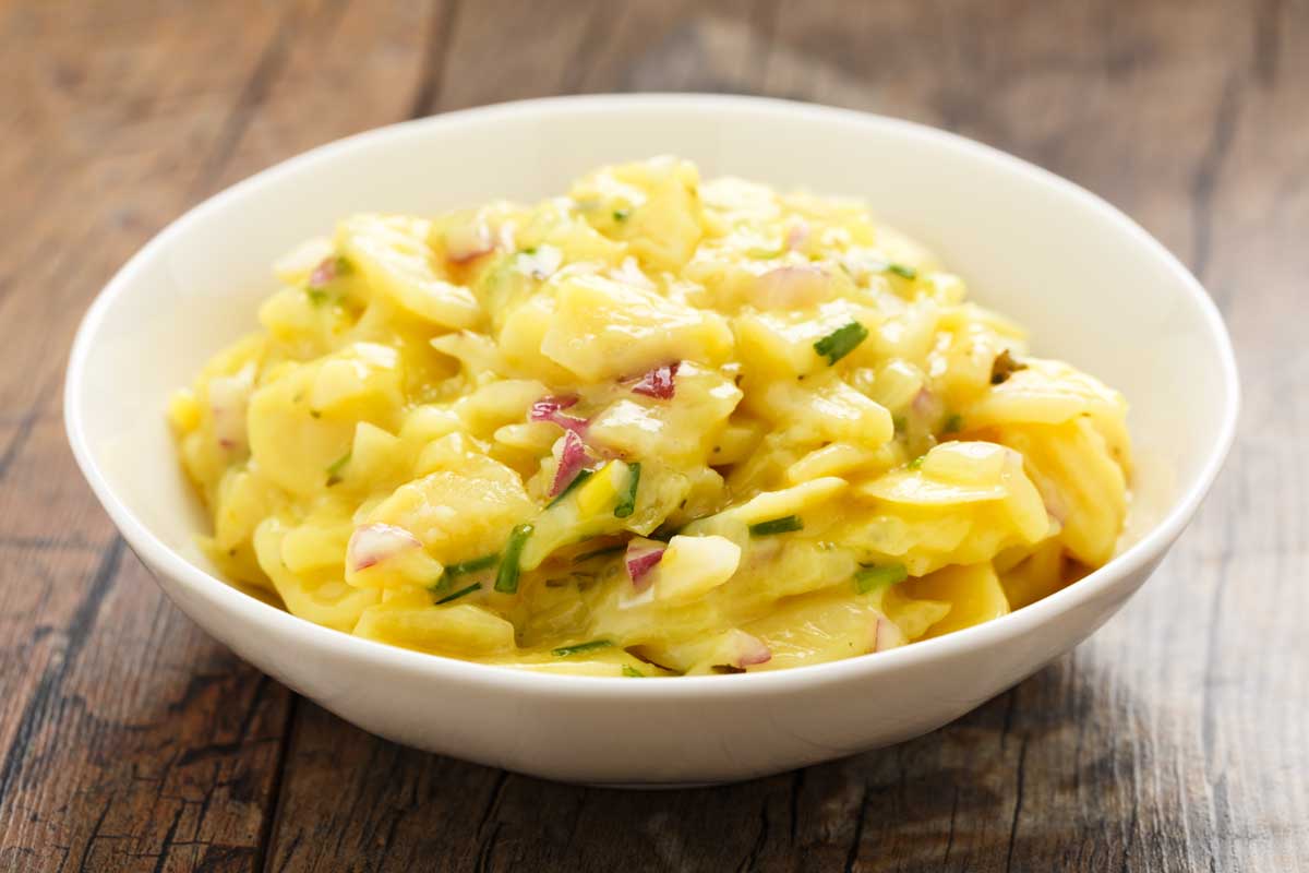 weisse Schuessel mit Kartoffelsalt mit kleinen Schinkenstueckchen und ein wenig Schnittlauf als Deko