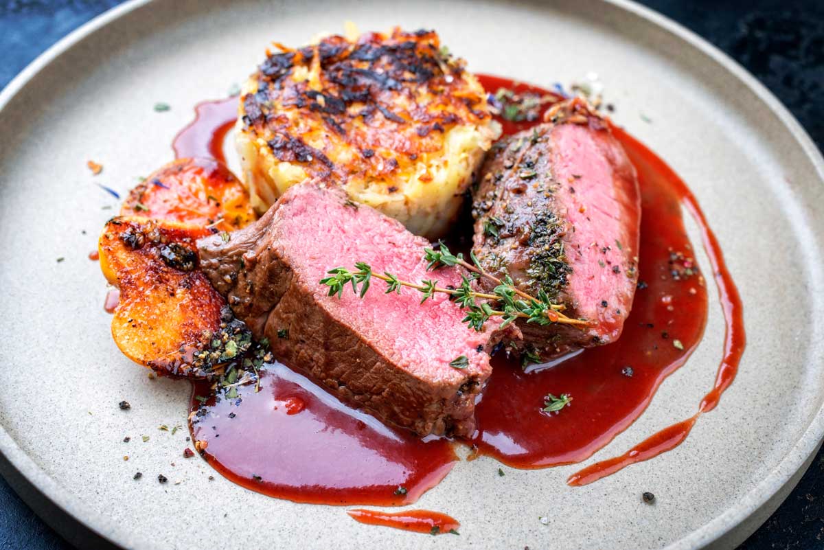 auf einem Teller zwei Scheiben Schweinebraten (medium gegart) mit Sherrysauce und zwei halben Kartoffelkloessen