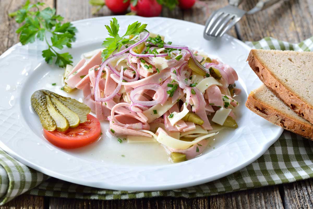 Wurstsalat auf weissem Teller mit Streifen von Schinkenwurst, Käse, Gurken und Zwiebeln