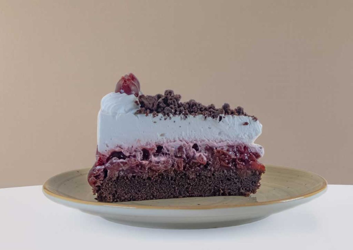 ein Stueck Schwarzwaelder Kirschtorte mit Schokoladenboden, Kirschschicht und Schlagsahne mit Kakao bestreut