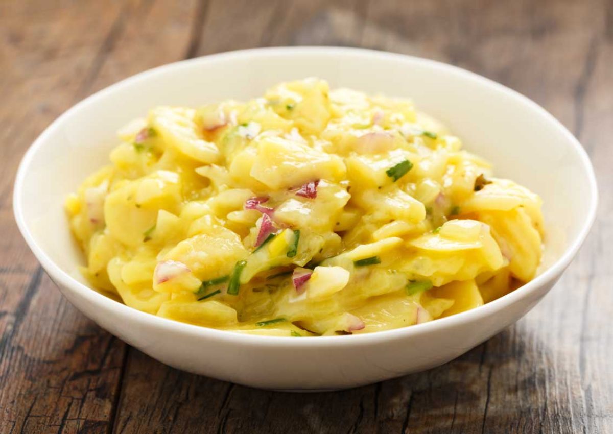 eine Schuessel mit Kartoffelsalat, kleinen Schinkenwuerfeln und Schnittlauch Dekoration