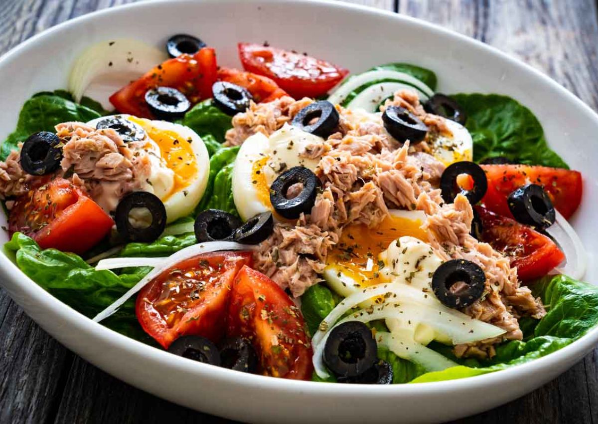 Salatschuessel mit Thunfischstuecken, Tomatenscheiben, gekochtem Eierscheiben, schwarzen Olivenscheiben, Sardellen und Kaese