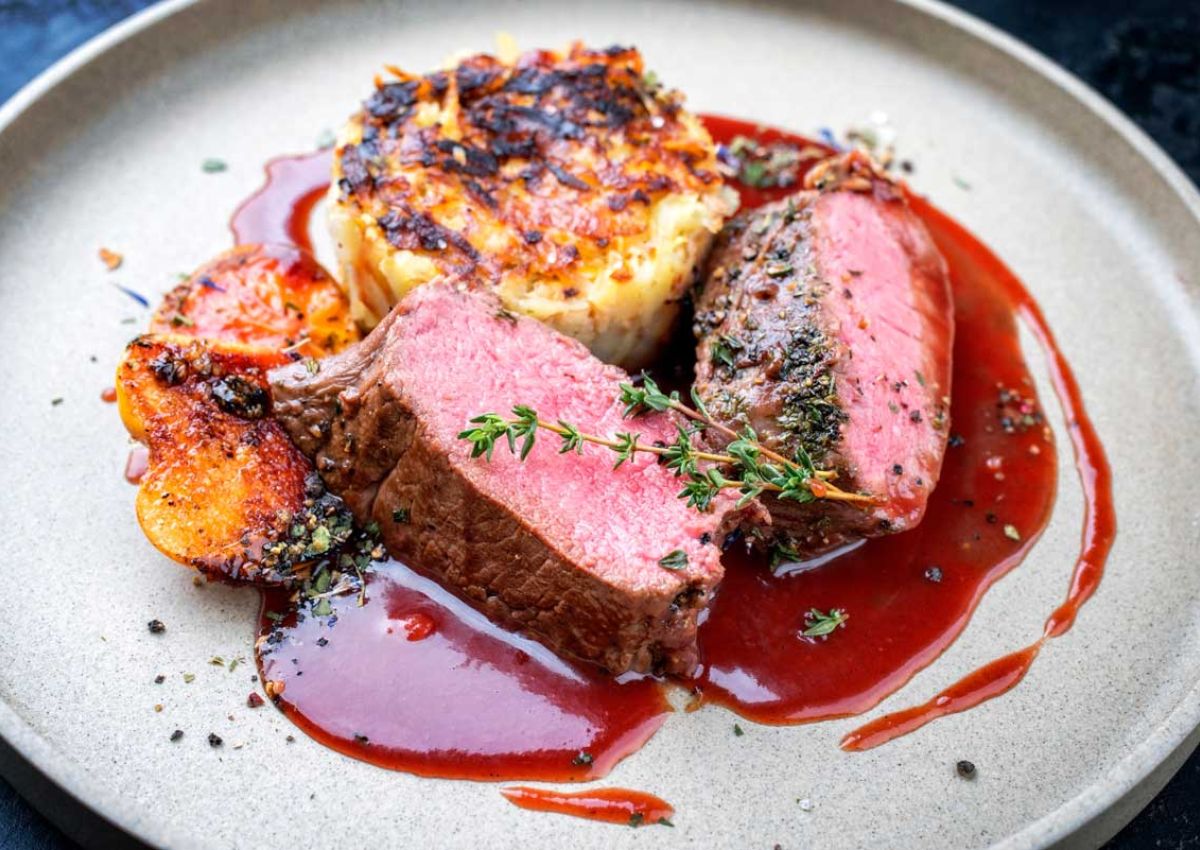 zwei Scheiben Schweinebraten medium gekocht mit halben Kartoffelkloessen und Cherry Orangen Sauce